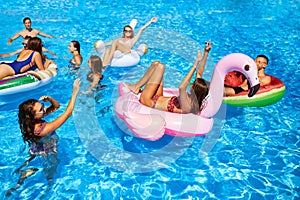 Friends having party in private holiday villa swimming pool. Happy young people swim on inflatable flamingo, swan at