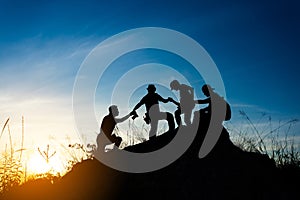 friends helping each other and with teamwork trying to reach the top of the mountains during wonderful summer sunset