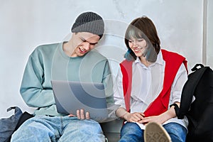 Friends hipster teenagers guy and girl sitting on floor with backpacks using laptop