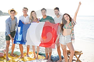 Friends holding French flag while standing at beach