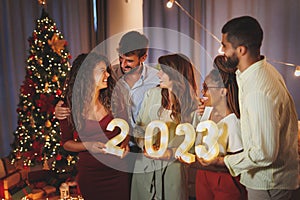 Friends holding illuminative numbers 2023 while celebrating New Year