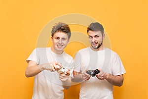 Friends with joysticks in their hands are on a yellow background, looking into the camera and playing video games. Two people play