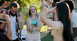 Friends laughing dance together on an RV trip to the lake. Young students people enjoying the outdoors drinking beer