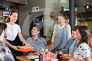 Friends looking at waitress serving food in restaurant