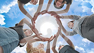 Friends make a circle from their palms against the background of a fabulous sky.