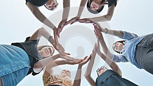 Friends make a circle with their palms against the blue sky.