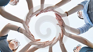 Friends make a circle with their palms against the blue sky.