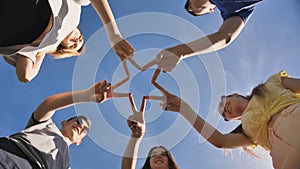 Friends make a star shape from their hands against a blue sky