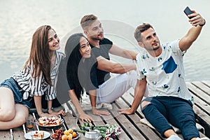 Friends making selfie sitting on pier with lake background while