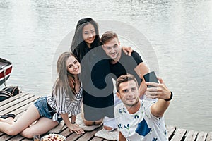 Friends making selfie sitting on pier with lake background while