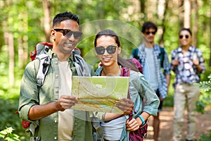 Friends with map and backpacks hiking in forest