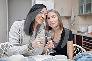 Friends meeting with wine and cake in the modern style kitchen. Young women smile and joke with glasses of wine in his hands