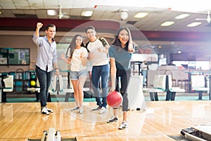 Friends Motivating Teen Girl Throwing Bowling Ball At Alley