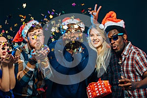 Friends at New Year`s party, wearing santa hats, dancing and blowing confetti