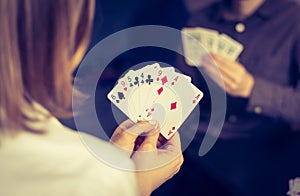 Friends are playing cards together at home. Woman is holding cards in her hands, man in the blurry background