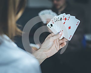 Friends are playing cards together at home. Woman is holding cards in her hands, man in the blurry background