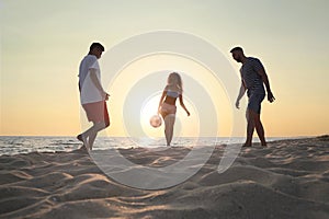 Friends playing football on beach at sunset