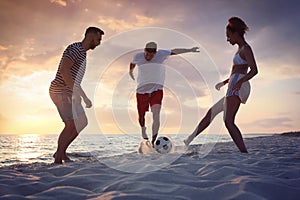 Friends playing football on beach at sunset