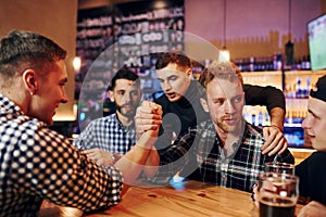 Friends plays arm wrestling. Group of people together indoors in the pub have fun at weekend time