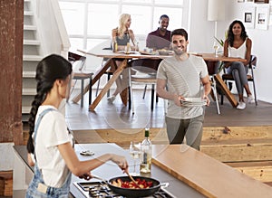 Friends Prepare And Serve Food For Dinner Party At Home Together