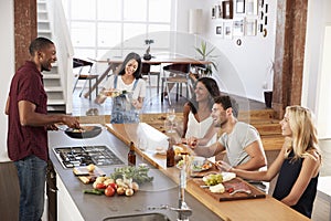 Friends Prepare And Serve Food For Dinner Party At Home Together