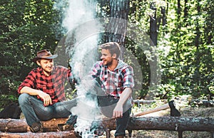 Friends relaxing near campfire after day hiking or gathering mushrooms. Company two male friends enjoy relaxing together