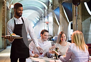 Friends in restaurant and black waiter