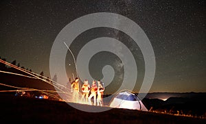 Friends resting beside camp, campfire under night starry sky