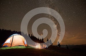 Friends resting beside camp, campfire under night starry sky