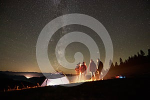 Friends resting beside camp, campfire under night starry sky