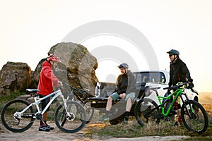 Friends Resting near Pickup Off Road Truck after Bike Riding in the Mountains at Sunset. Adventure and Travel Concept.