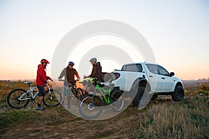 Friends Resting near Pickup Off Road Truck after Bike Riding in the Mountains at Sunset. Adventure and Travel Concept