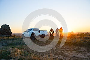 Friends Riding Bikes in the Mountains in front of the Pickup Off Road Truck at Sunset. Adventure and Travel Concept