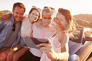 Friends On Road Trip Sit On Convertible Car Taking Selfie