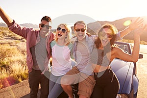 Friends On Road Trip Sitting On Hood Of Convertible Car