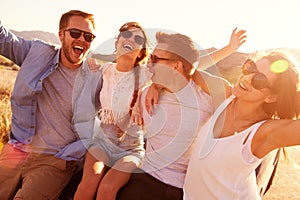 Friends On Road Trip Sitting On Hood Of Convertible Car