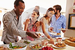 Friends serving themselves food and talking at dinner party