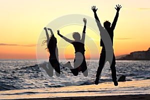 Friends silhouette jumping happy on the beach at sunset