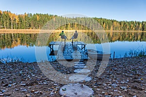 Friends sit in chairs on a dock on the shore of the lake. Autumn landscape