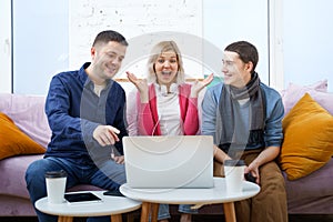 Friends sit on the couch, chatting and using a smartphone, desktop computer, laptop.