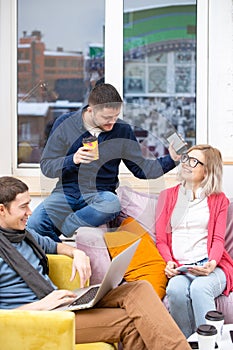 Friends sit on the couch, chatting and using a smartphone, desktop computer, laptop.