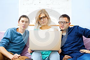 Friends sit on the couch, chatting and using a smartphone, desktop computer, laptop.