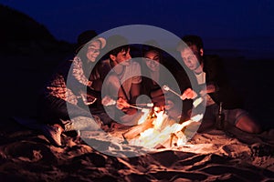 Friends sitting on the beach clink glasses near bonfire