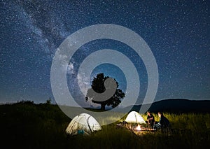 Friends travellers spending time in the mountains sitting around bonfire in camping under beautiful starry sky