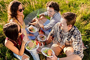 Friends sitting in grass and having burgers at barbecue party