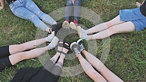 Friends are sitting on the grass with their legs joined in a circle.