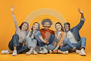 Friends sitting and raising hands joyfully on orange background