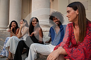 Friends are sitting on a staircase and meet to chat, girls and a boy of different ethnicity together