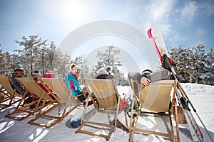 Friends on skiing sunbathing in sunbed on ski terrain, back view