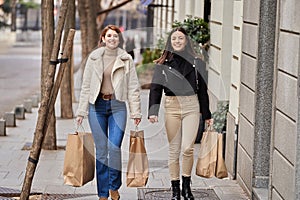 Friends smiling while walking down the street with shopping bags.